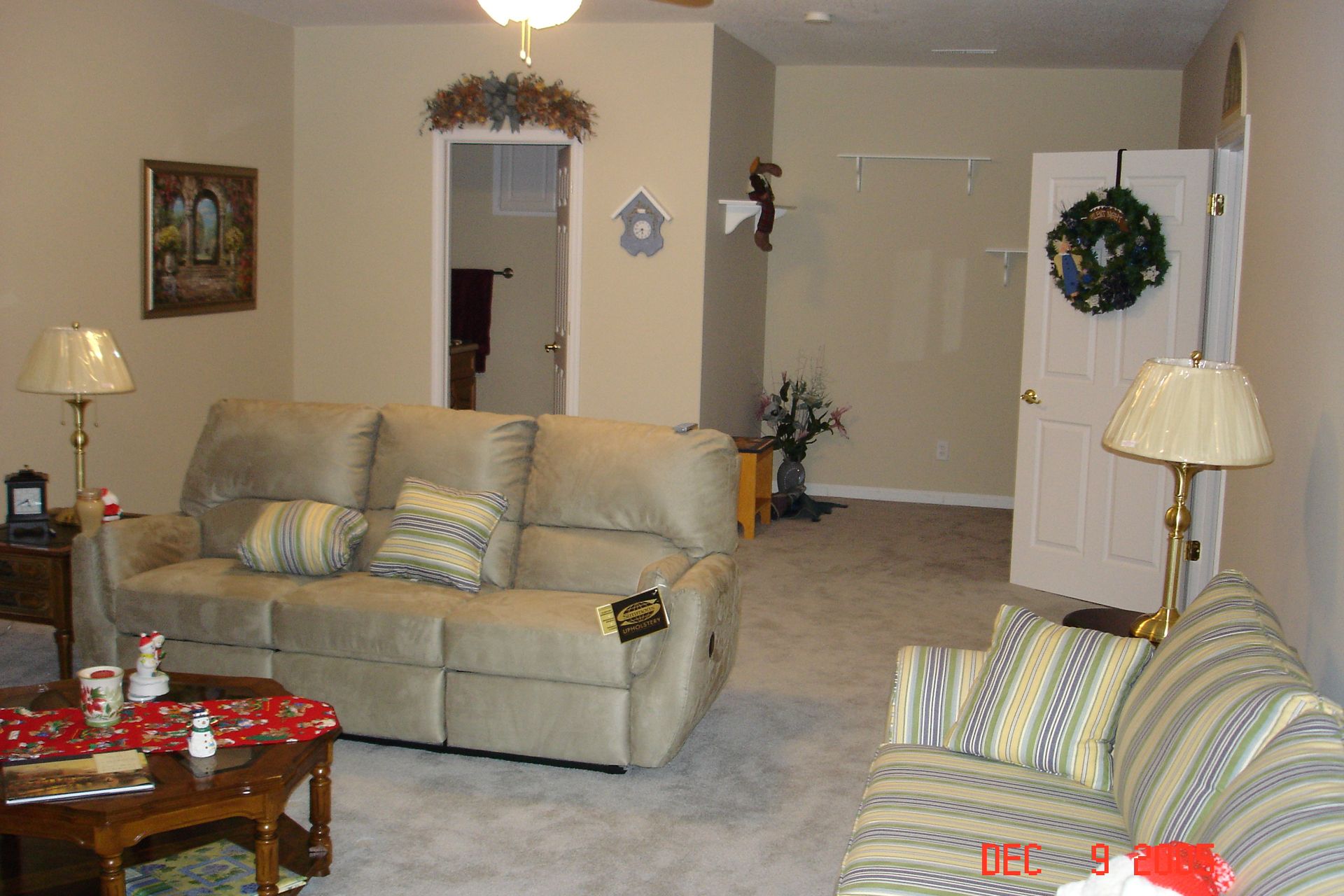 Living room with tan walls, couches, lamps, door with wreath, and small table.