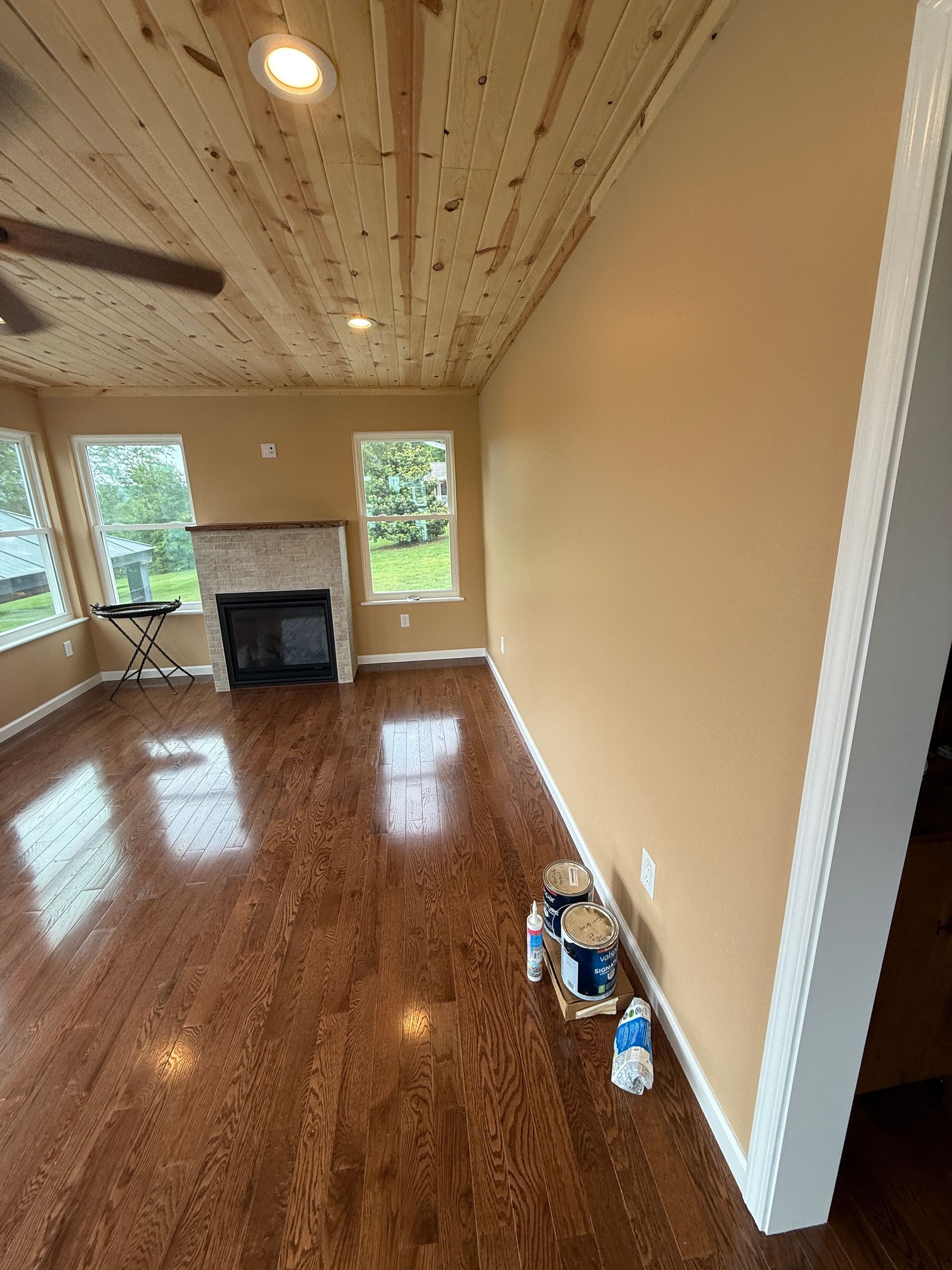 Living room with wood floor and ceiling, tan walls, fireplace, and windows.