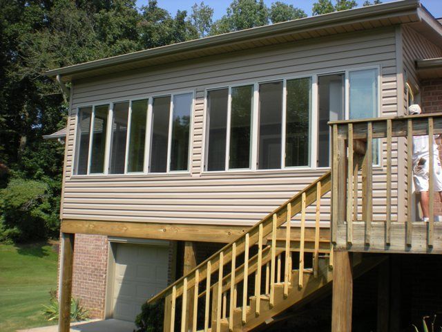Sunroom with multiple windows, attached to a deck with stairs. Beige siding, wooden deck and stairs.
