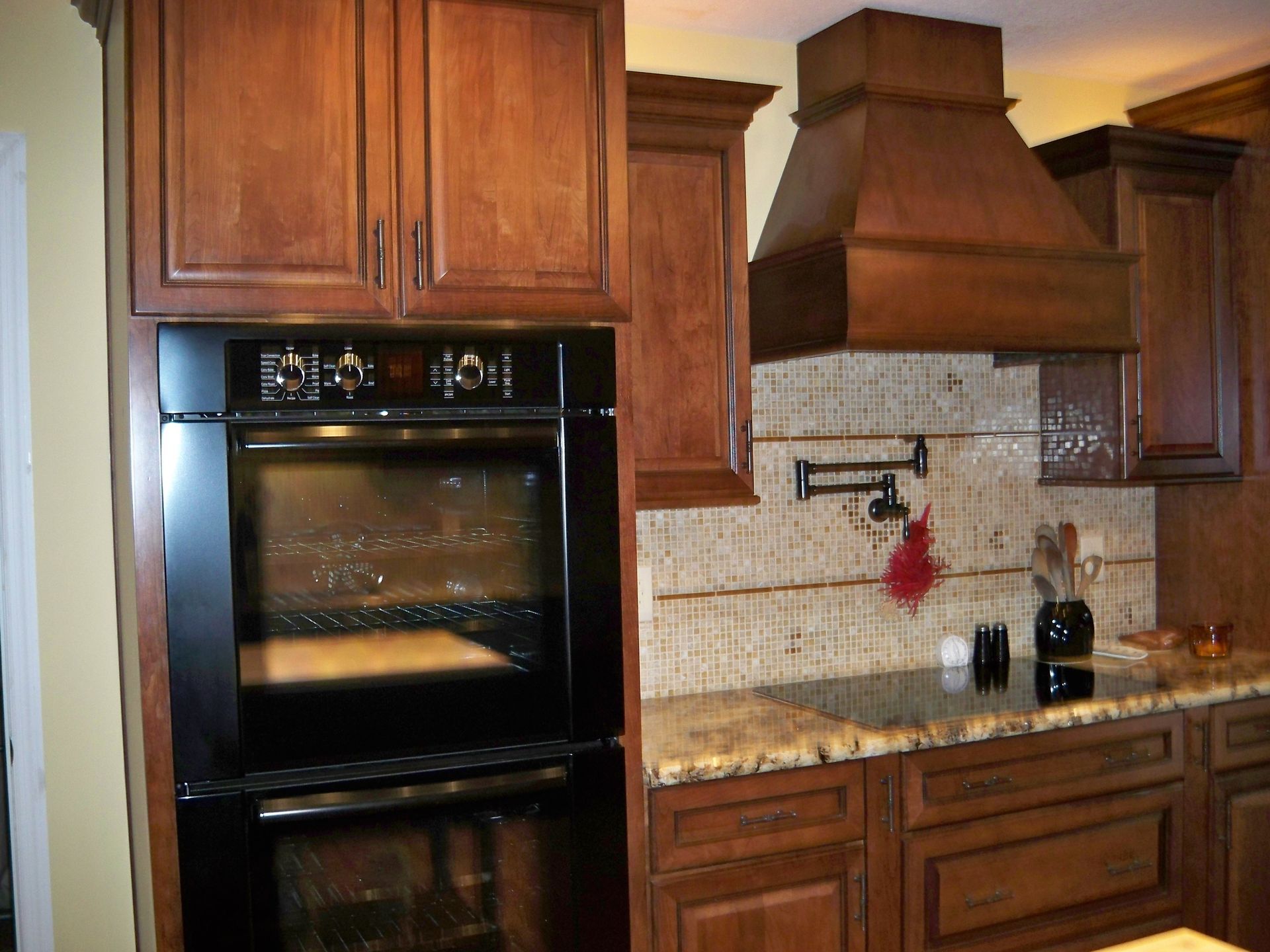 Dark wood kitchen with built-in oven, range hood, and speckled countertops.
