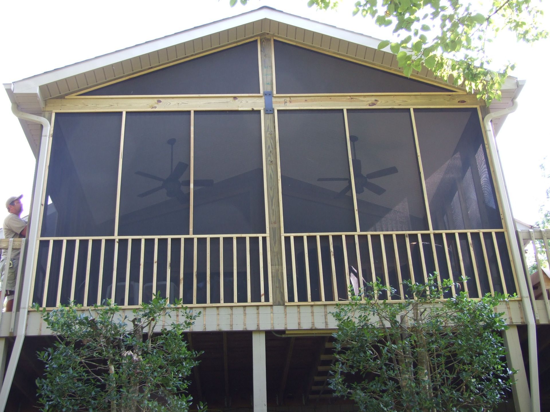 Screened porch with wooden frame, railings, and black screening, attached to a house.