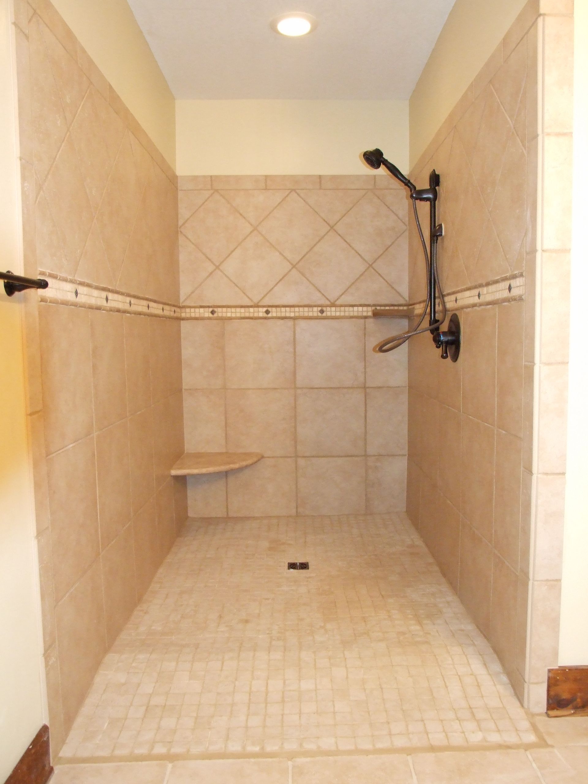 Walk-in shower with tan tiles, showerhead, and a small built-in seat.
