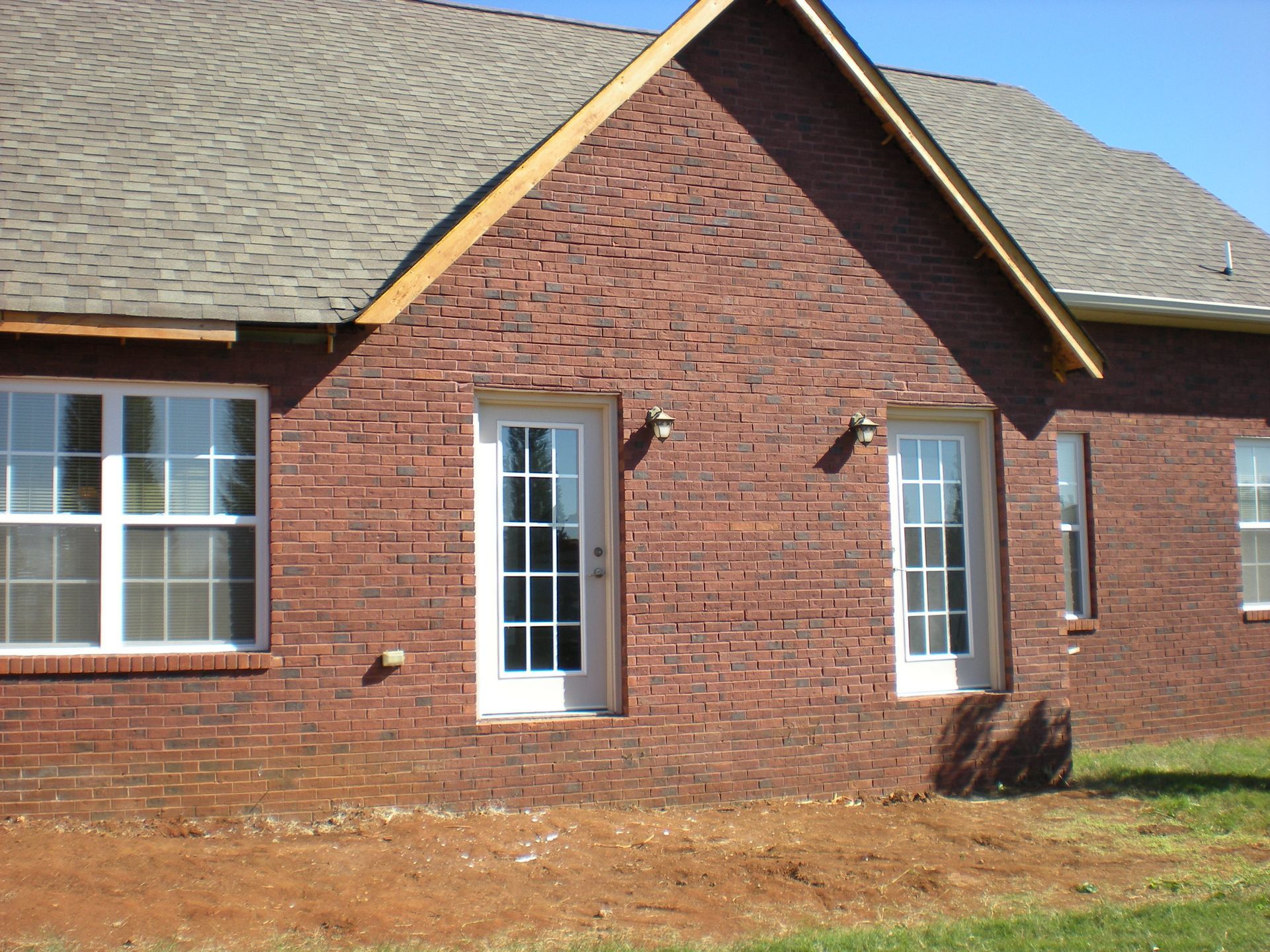 Red brick house exterior with white windows and doors; grey roof.