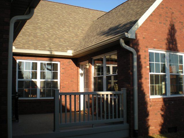 Brick home exterior with porch, windows, and brown roof under a sunny sky.