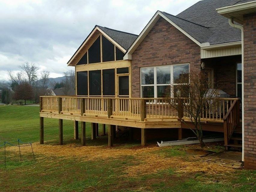 Wooden deck and screened-in porch attached to a brick house on a cloudy day, with a grassy yard.