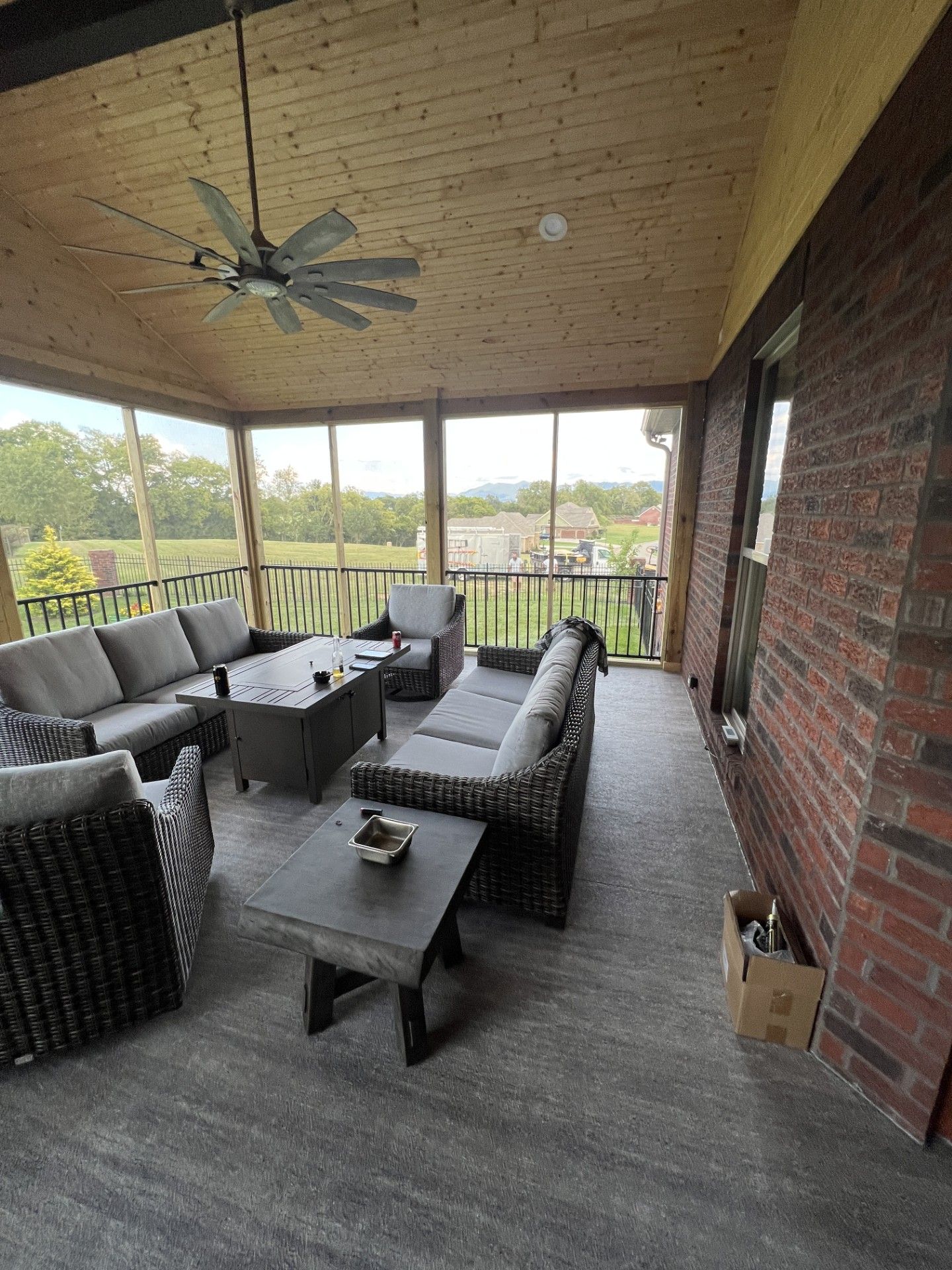 Screened-in porch with gray furniture, a ceiling fan, and brick wall. Overlooks a green yard and distant mountain.