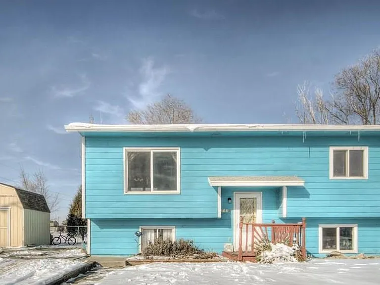 Bright blue house with snow-covered yard, small shed, and clear blue sky.