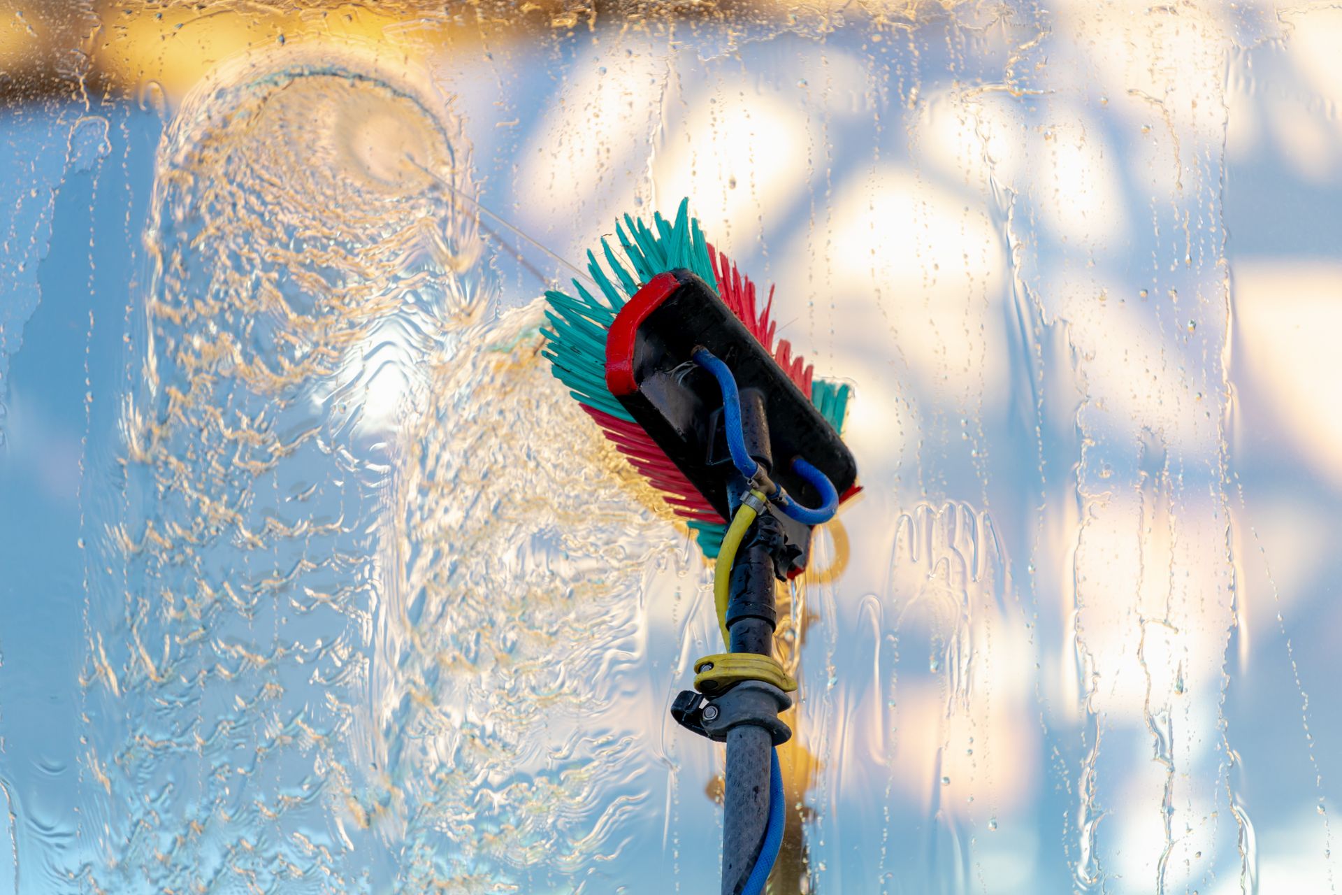 Close-up of a squeegee scraping water from a window, with frost and sunlight in the background
