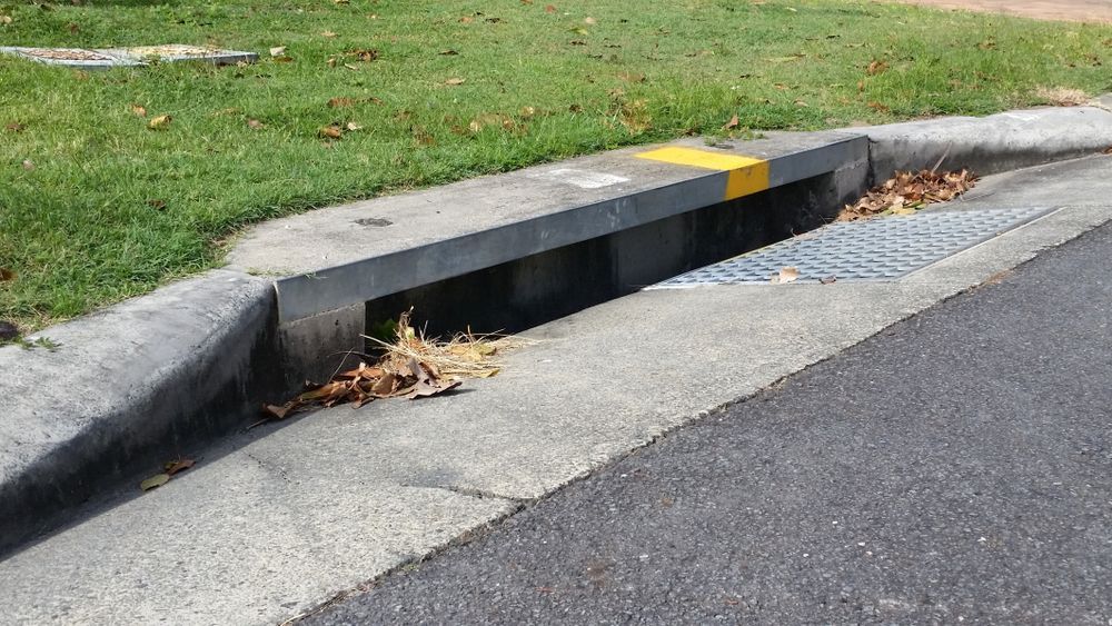 A drain on the side of a road next to a grassy area— Subat Plumbing Services in Cessnock, NSW