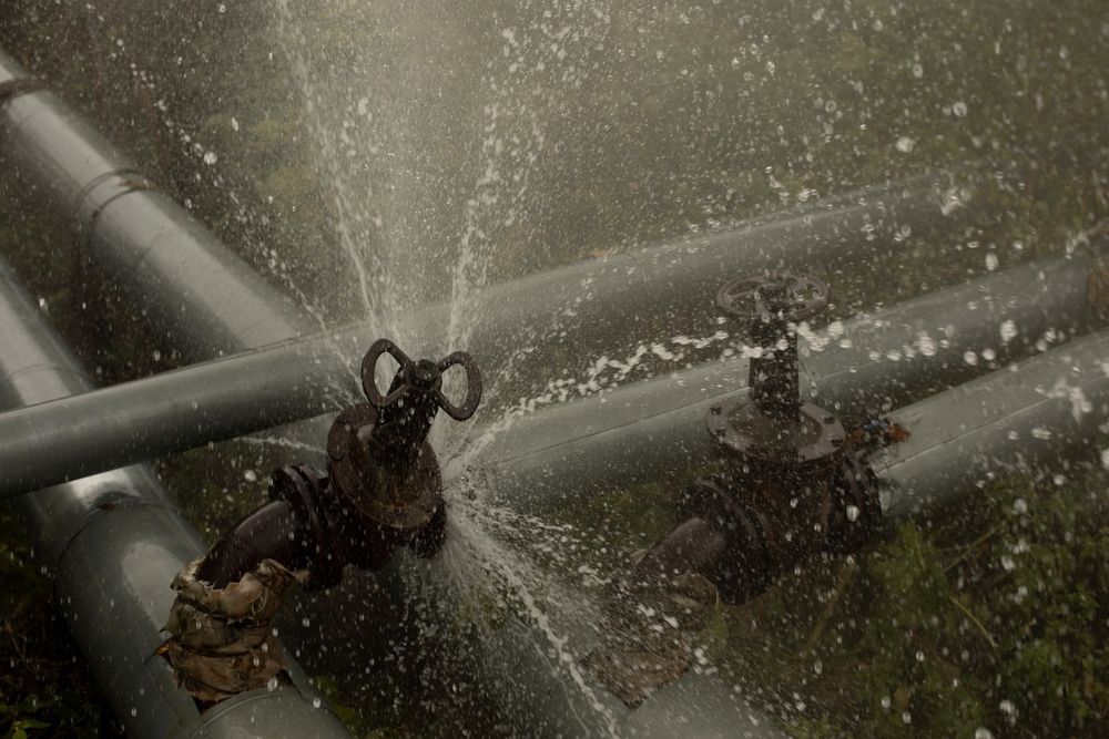 A Sprinkler is Spraying Water From a Pipe in the Rain — Subat Plumbing Services in Kurri Kurri, NSW