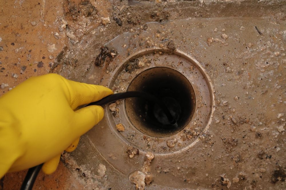 A Person Wearing Yellow Gloves is Cleaning a Drain With a Hose — Subat Plumbing Services in Cessnock, NSW