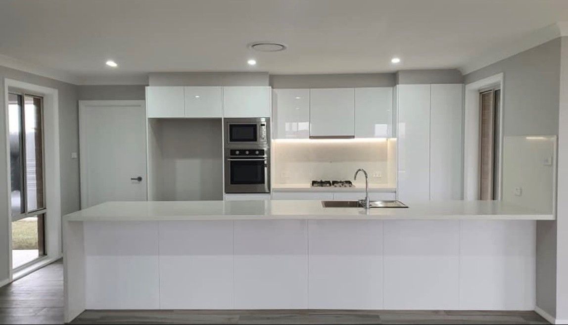 A Kitchen With White Cabinets, Stainless Steel Appliances, and a Large Island — Subat Plumbing Services in Kurri Kurri, NSW