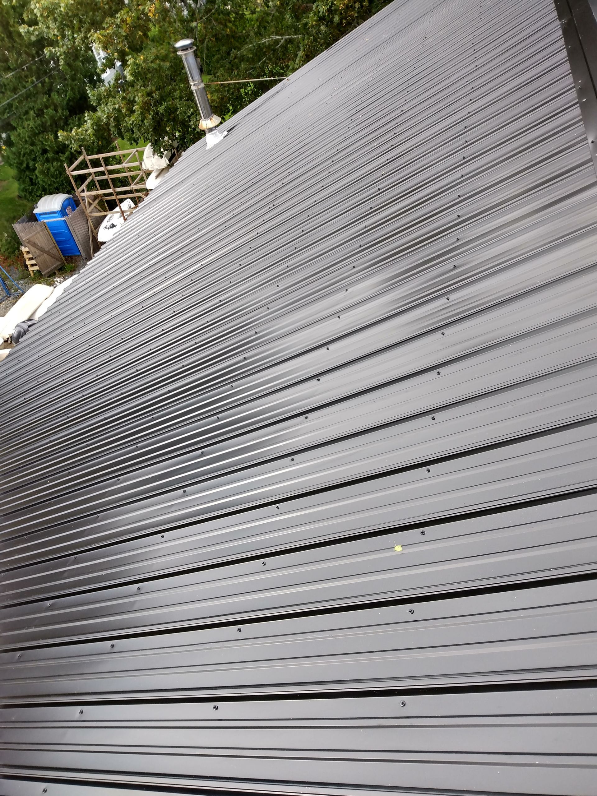 High-angle view of a dark, ribbed metal roof with a chimney, viewed from above.