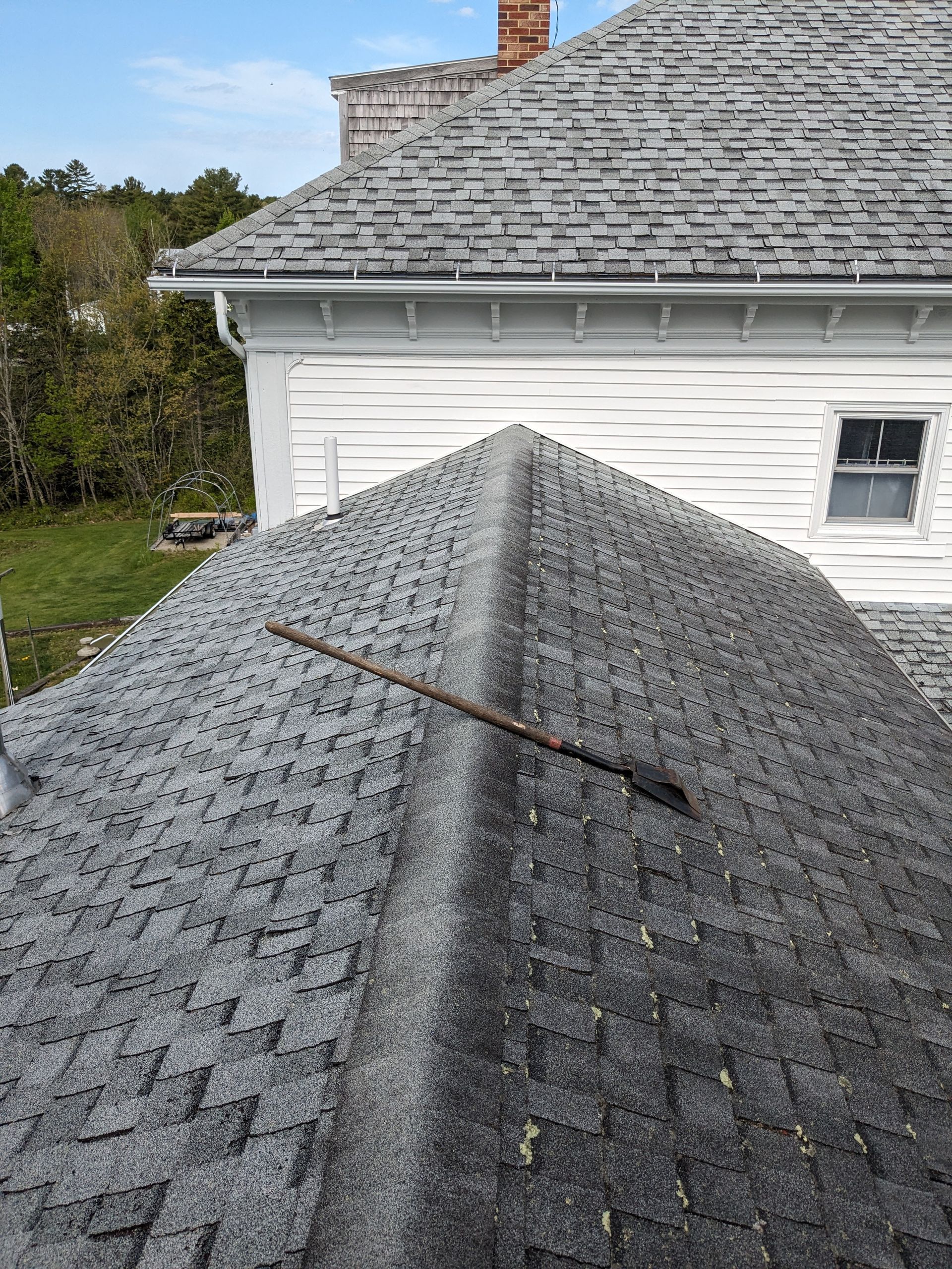 A rusted metal tool, possibly a shovel, lies diagonally across the peak of a gray shingled roof under a clear blue sky.