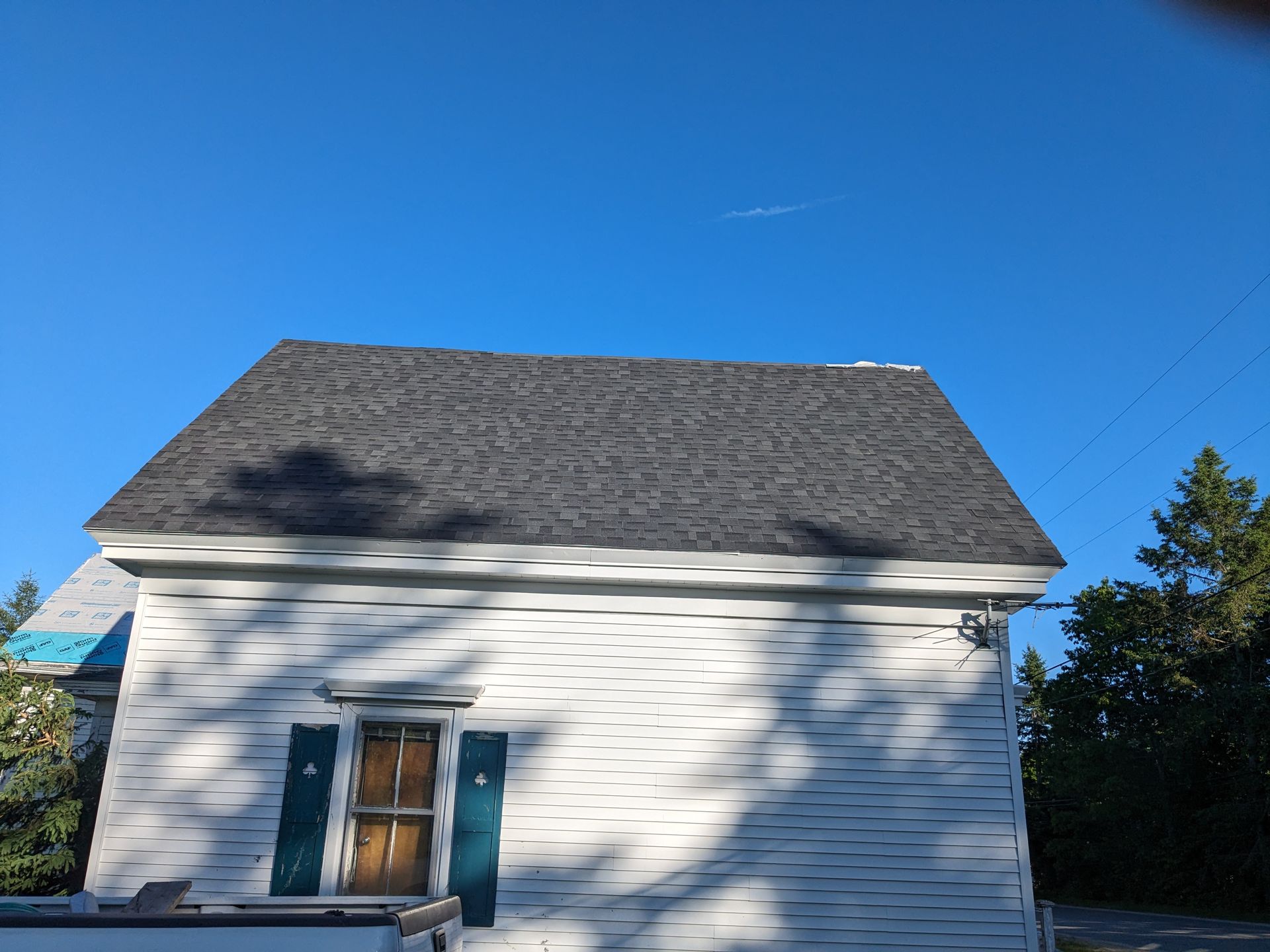 A white house with a new grey shingled roof and blue shutters against a clear blue sky.