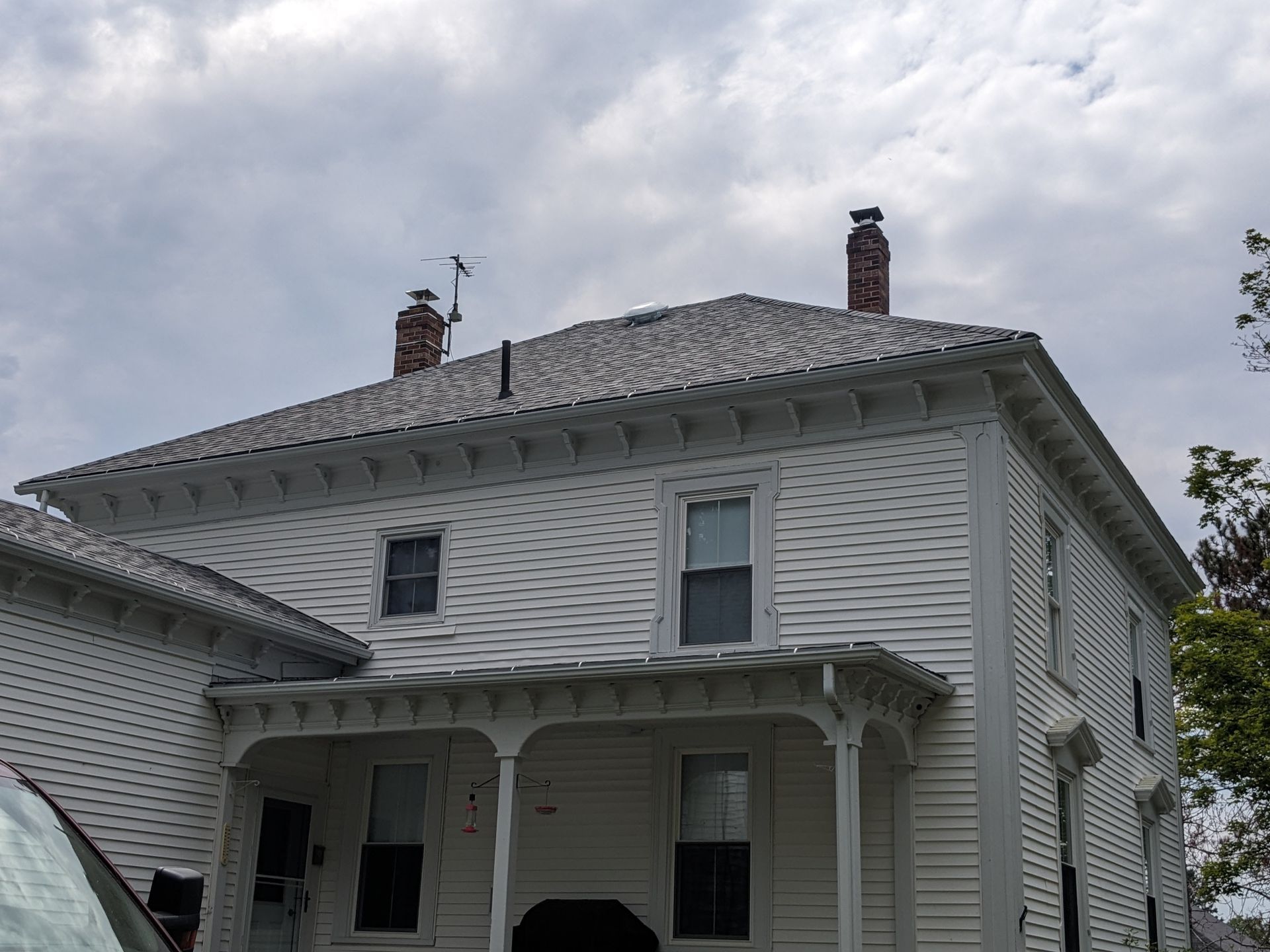 A two-story, white clapboard house with a covered front porch, decorative eaves, and two brick chimneys under a cloudy sky.