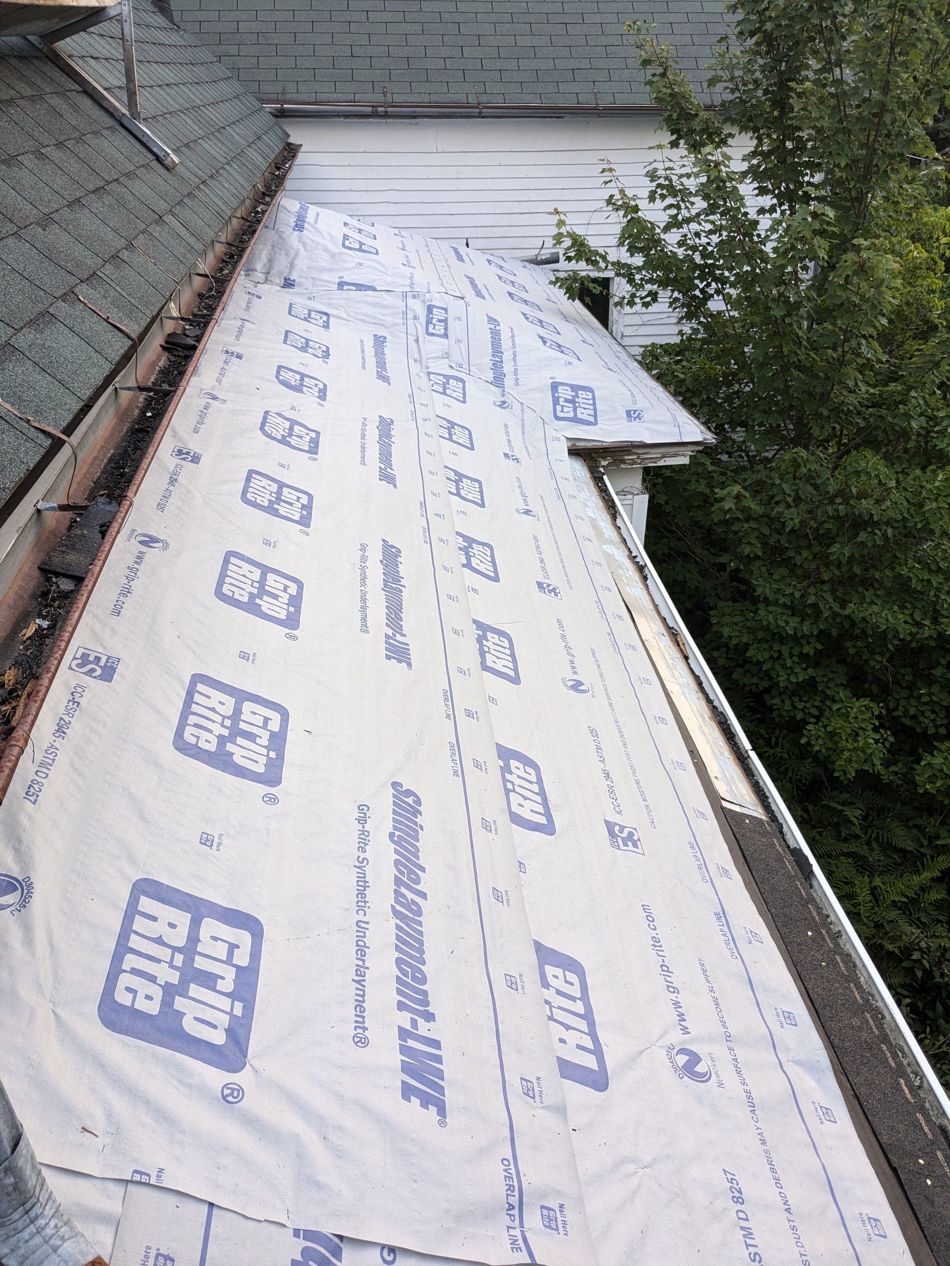 A section of a residential roof under construction, covered with white Grip-Rite synthetic underlayment.