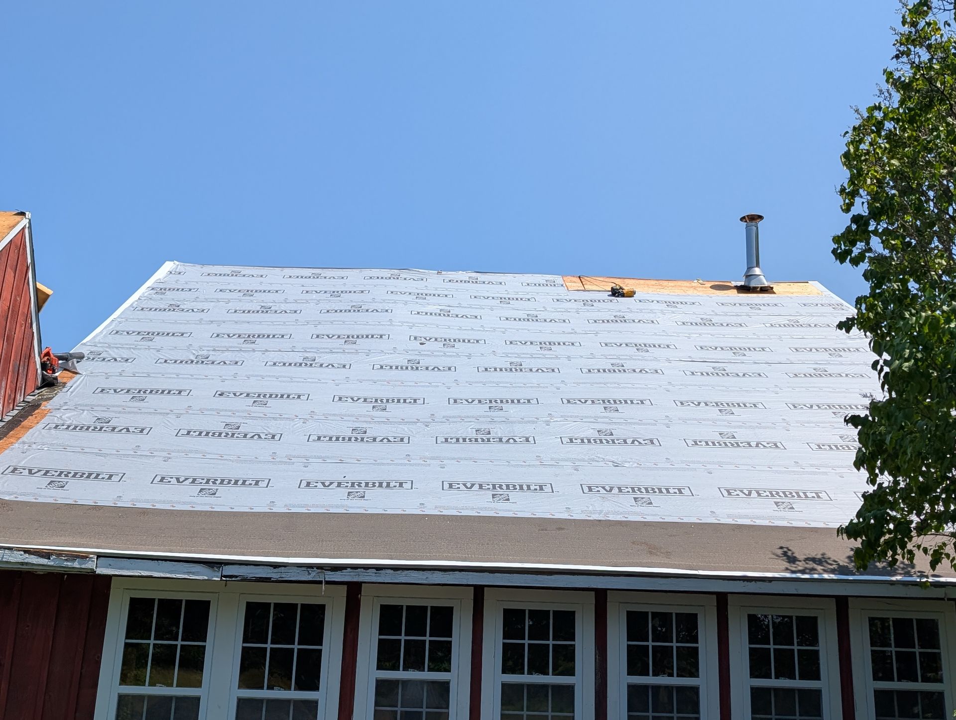 A house roof under construction, featuring new grey underlayment and a chimney, with windows visible below.