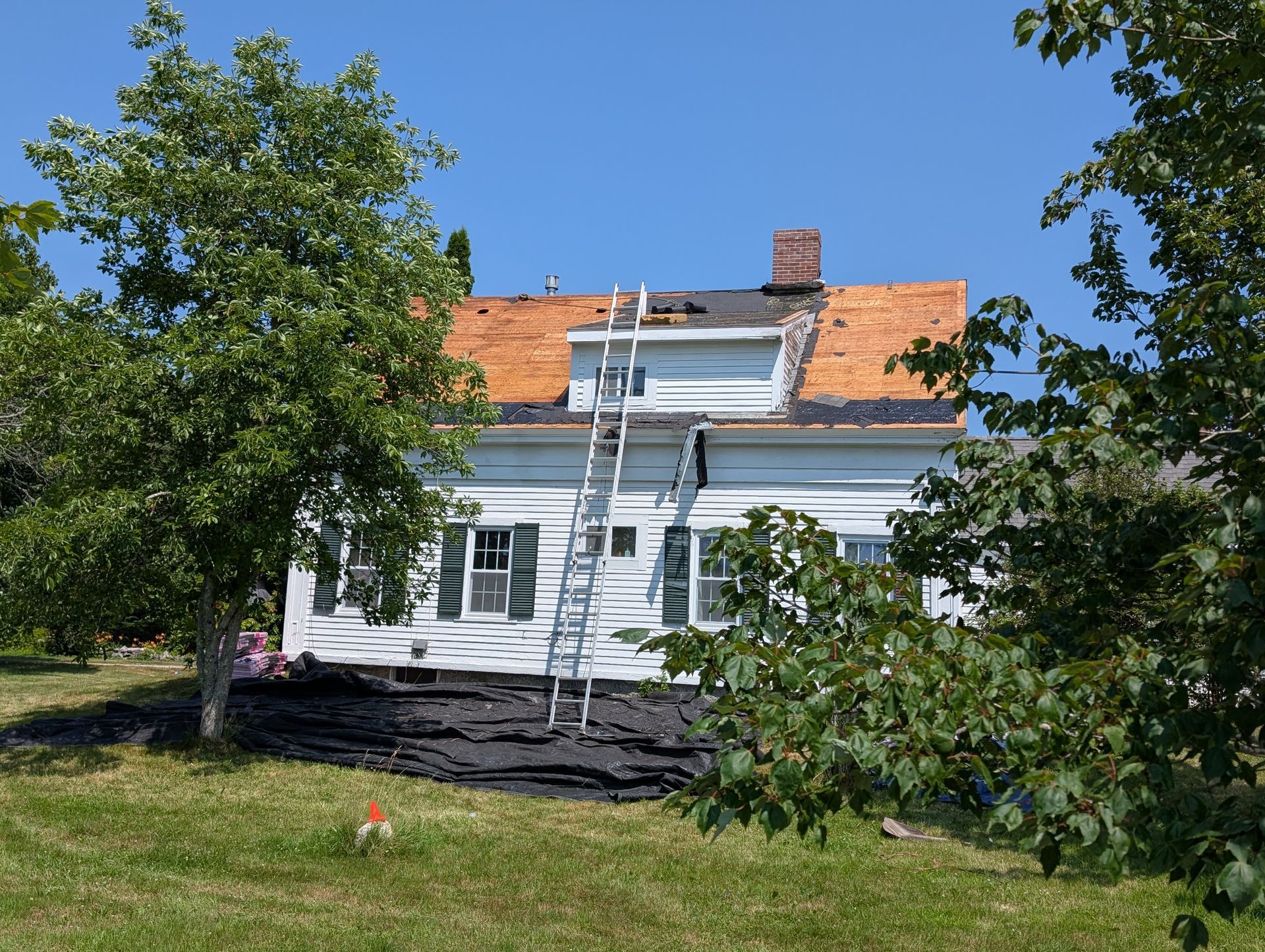 A white house under renovation with an extension ladder leaning against the roof and dark debris covering the front lawn.