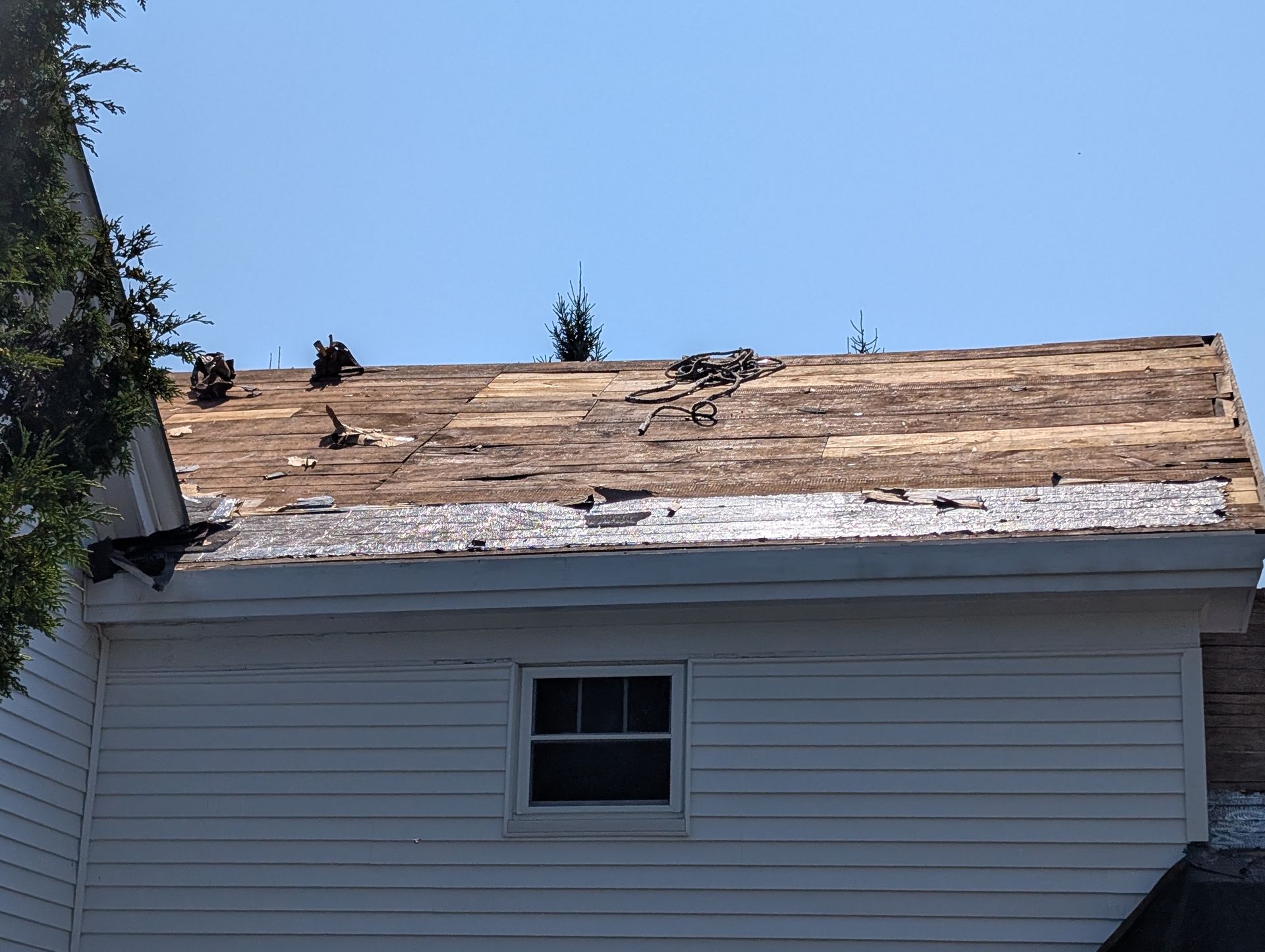 A residential roof with missing shingles, exposing the wooden deck and underlayment in broad daylight.