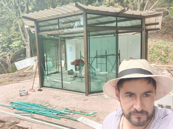 Un hombre con sombrero se toma selfis con la construcción de una estructura de vidrio