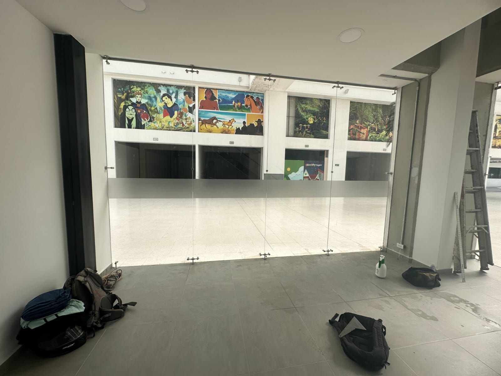 Vista interior de una tienda con grandes ventanales. Detrás de ellos se exhiben obras de arte coloridas.