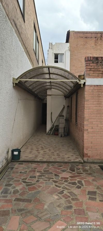 Pasarela cubierta entre edificios; suelo de ladrillo y piedra.