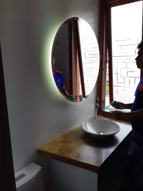Baño con espejo redondo, lavabo y ventana para limpiar. La luz se refleja alrededor del espejo.