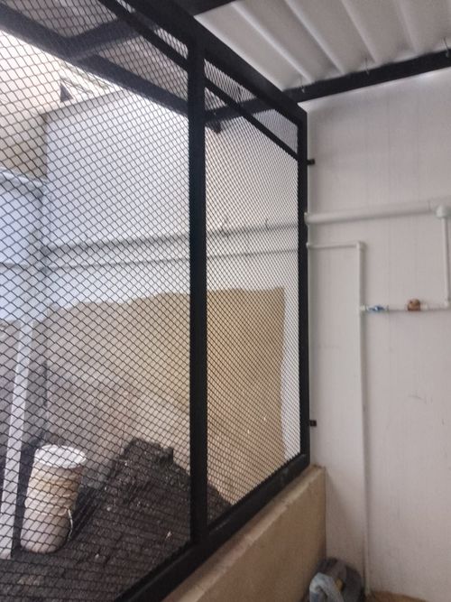 Jaula de metal de color negro con paredes de malla, probablemente para corral de animales, fijada a una pared.