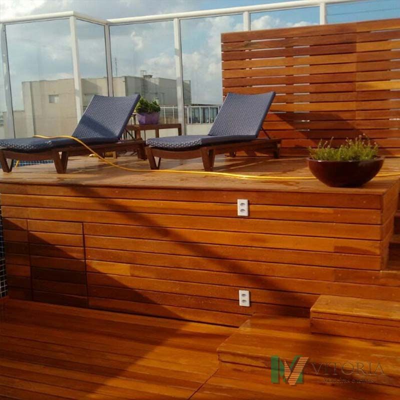 Terraço de madeira com espreguiçadeiras, divisória para privacidade e plantas, em um terraço.