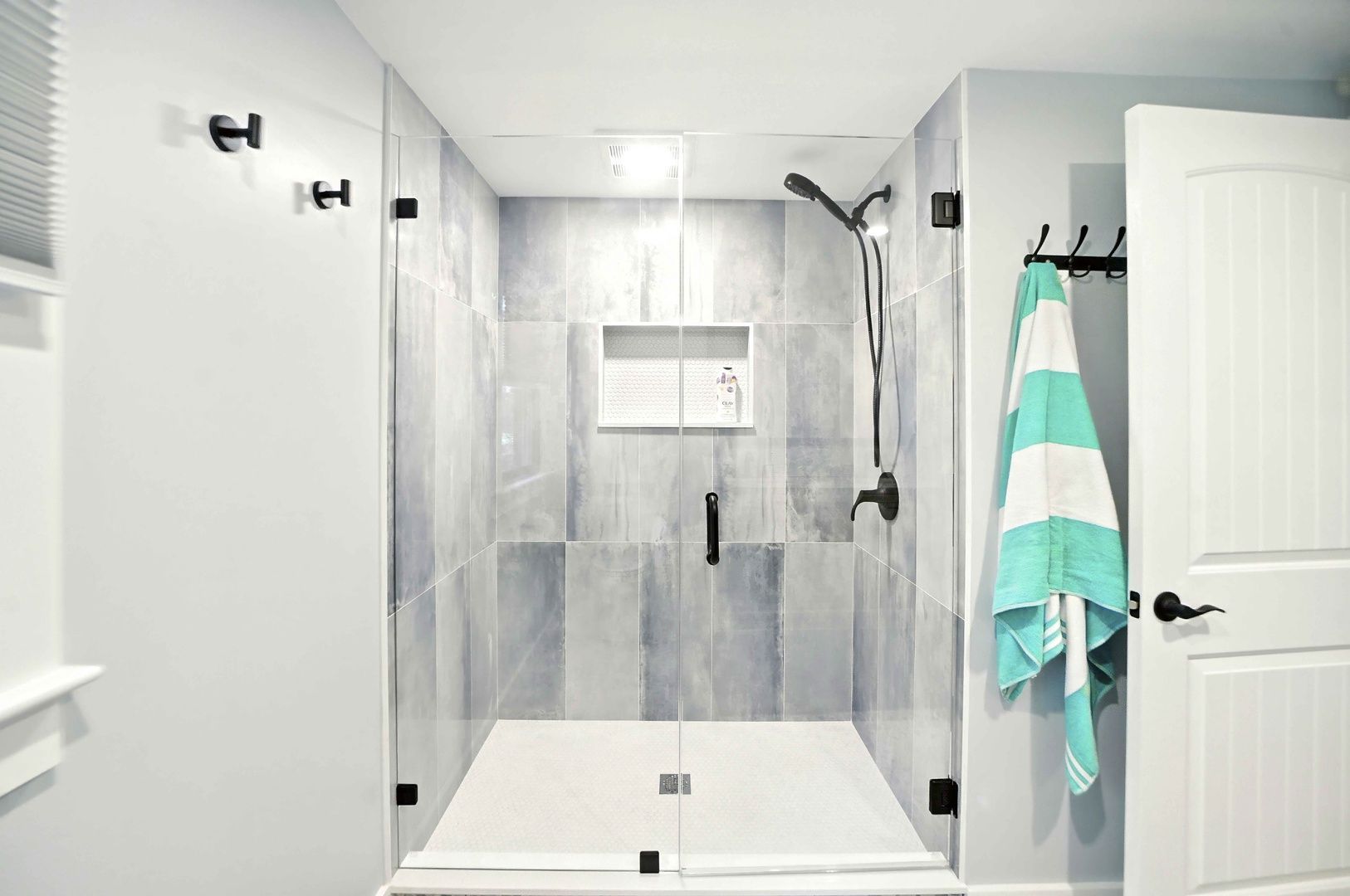 Modern bathroom with tiled shower, bench, towel hook, and open door