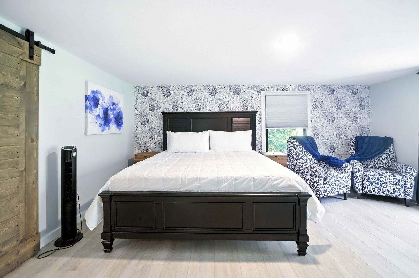 Bright bedroom with a dark bed, floral wallpaper, blue chairs, and a rustic sliding door