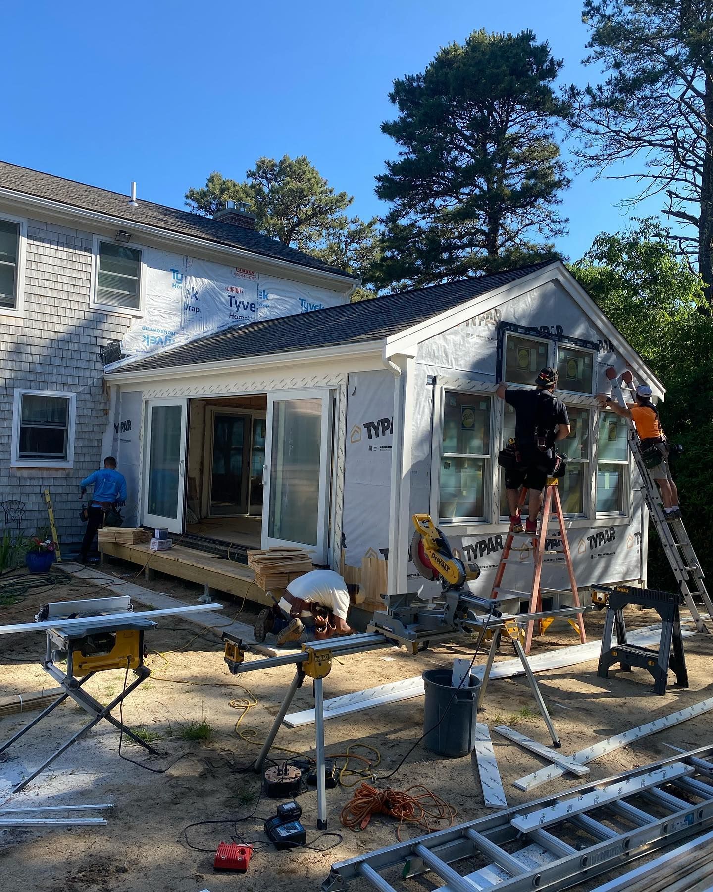 Workers renovating a house exterior, with ladders, tools, and scaffolding in the yard.