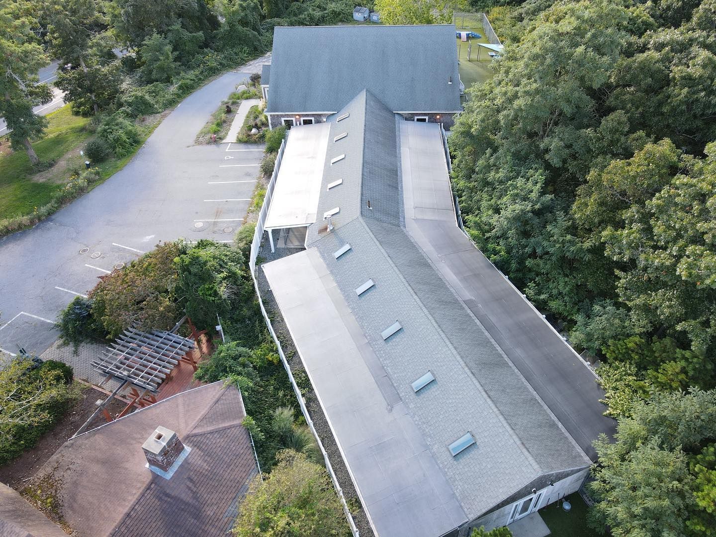 Aerial view of a curved gray-roofed building beside a parking lot and trees