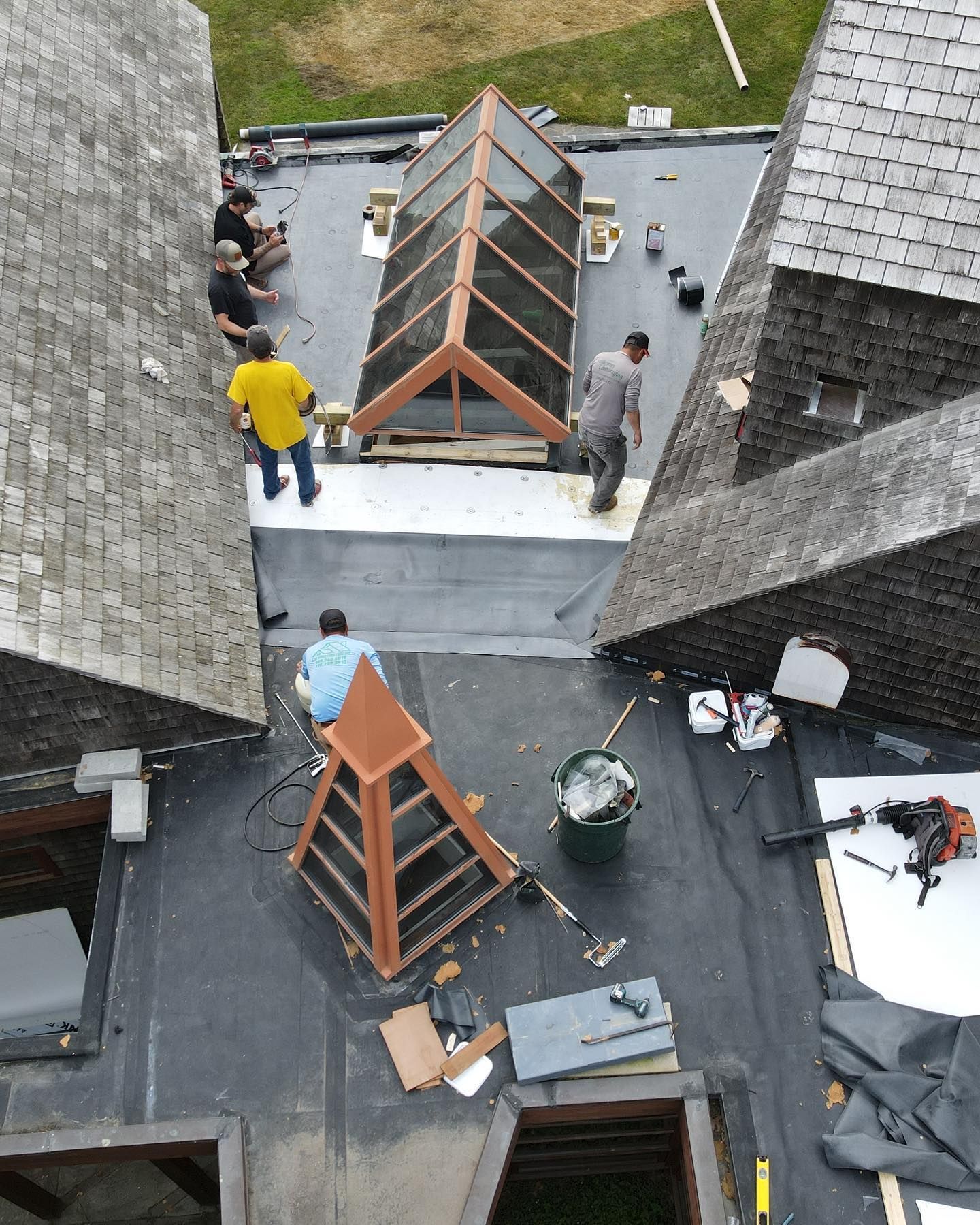 Roof workers assembling wooden skylight frames on a flat rooftop between slate buildings.