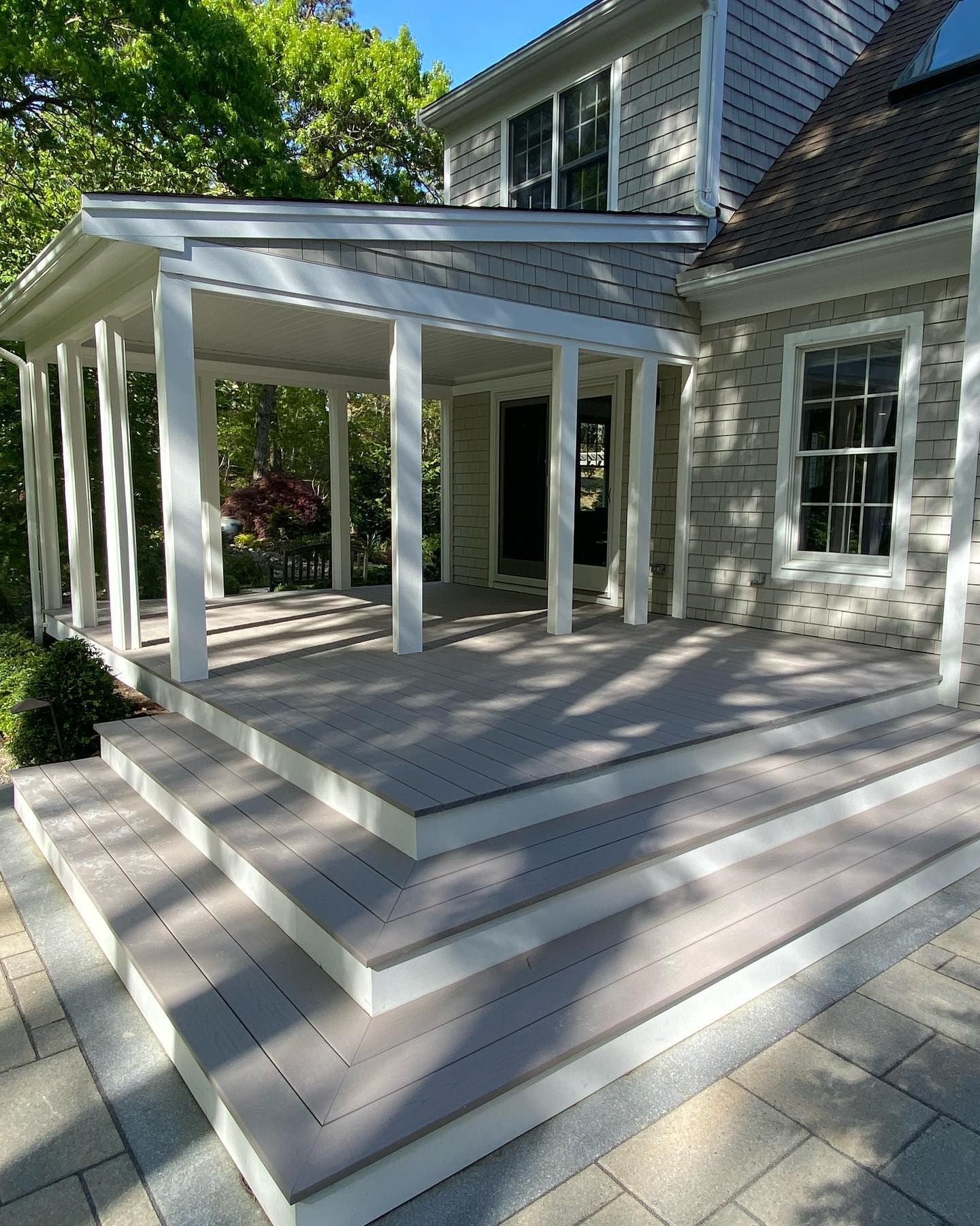 White house patio with steps, covered porch, and French doors in a sunny landscaped yard