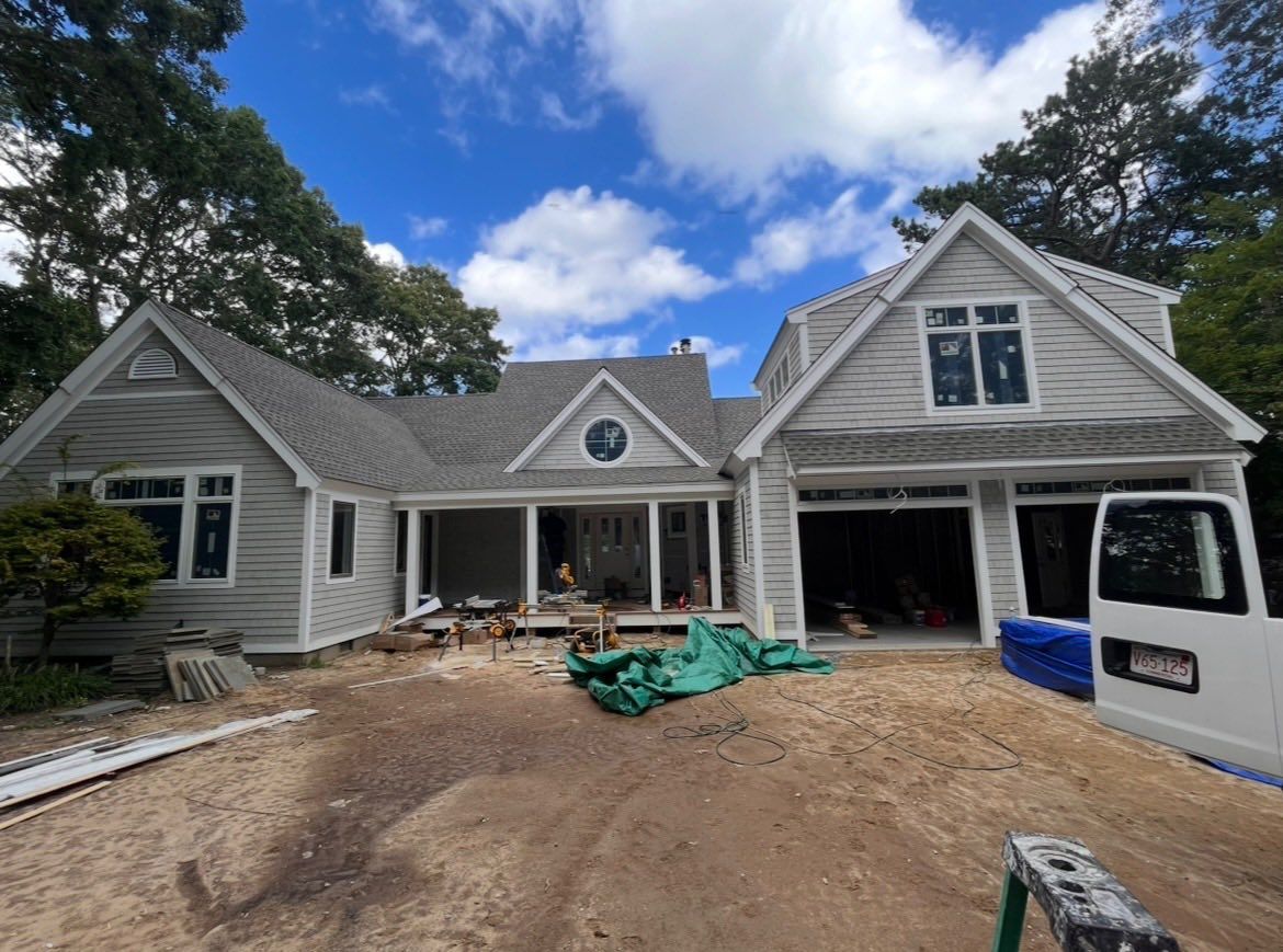 House under renovation with unfinished driveway, construction debris, and a van parked outside under a blue sky