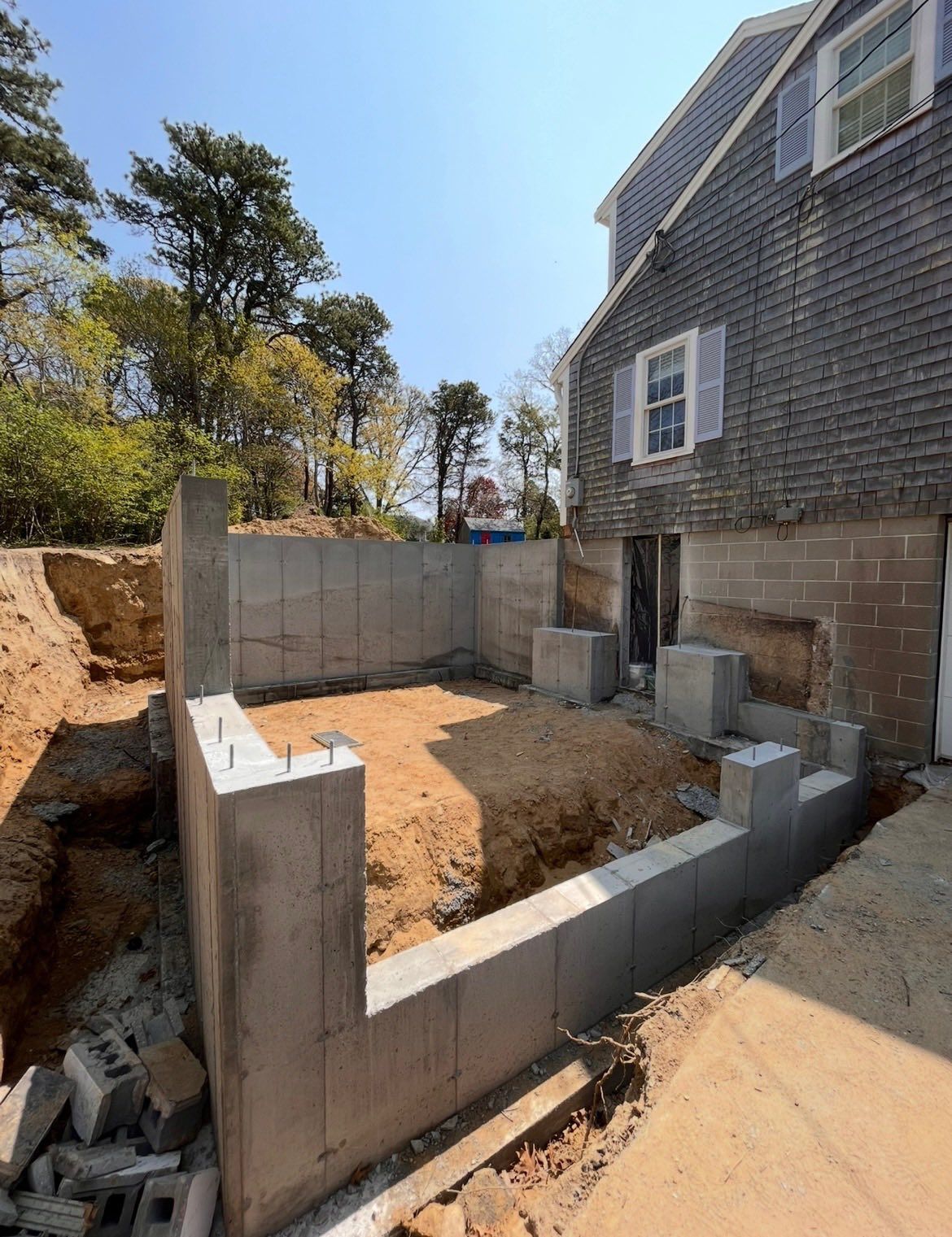 Partially built concrete foundation beside a gray house on a dirt construction site