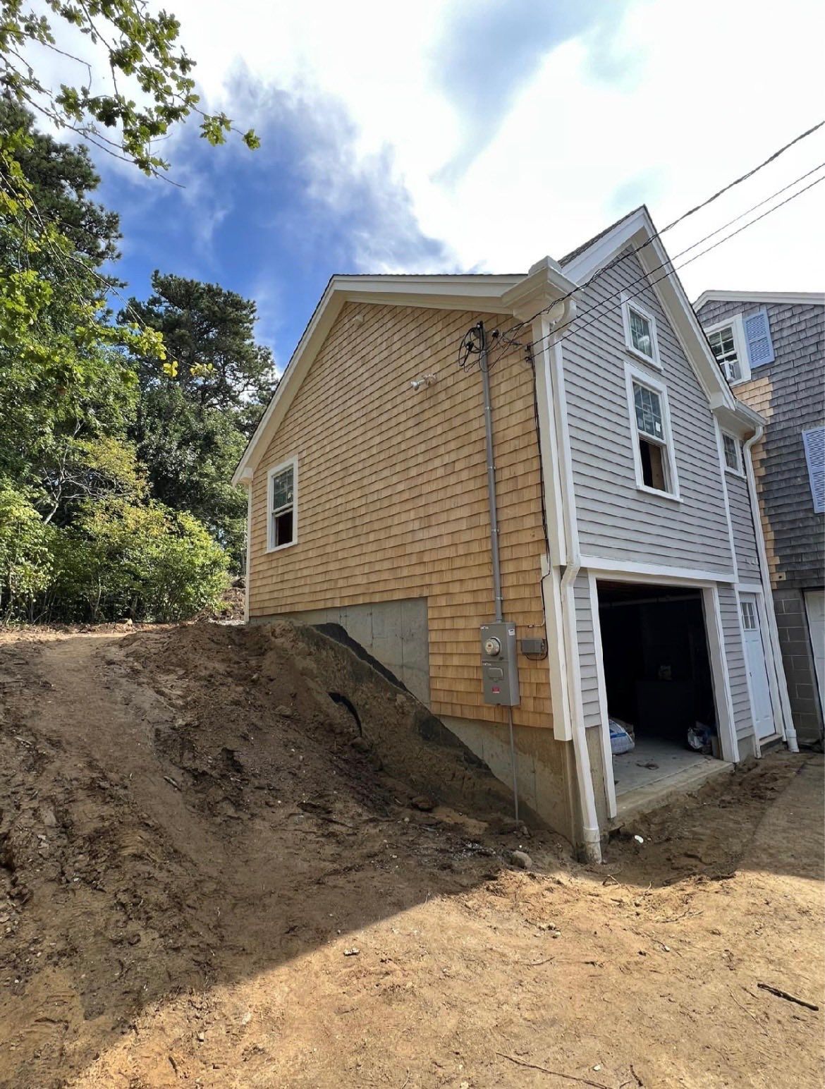 Partially built beige house with open garage on a dirt lot beside a steep hillside