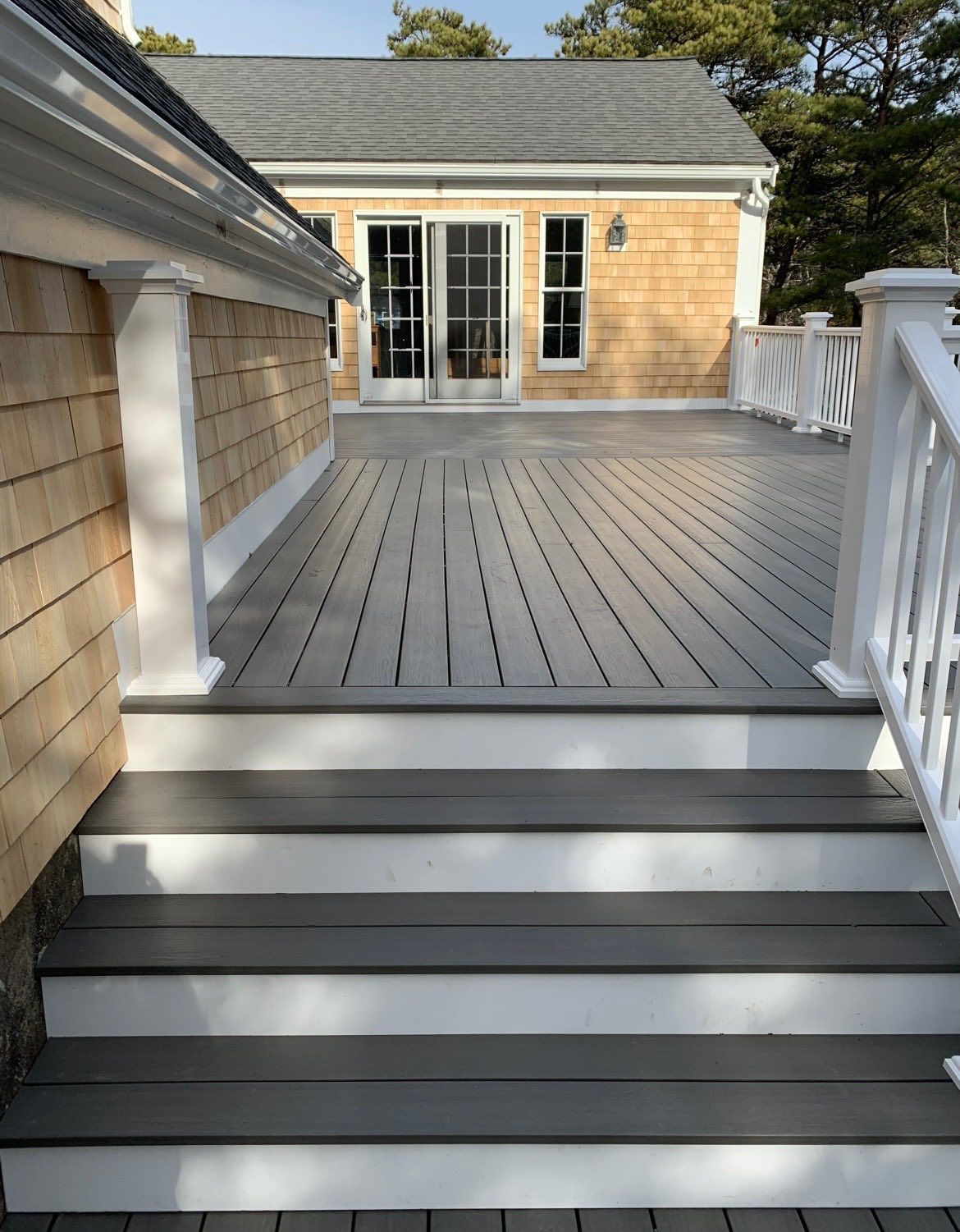 Gray backyard deck with white railings and steps leading to French doors on a tan house