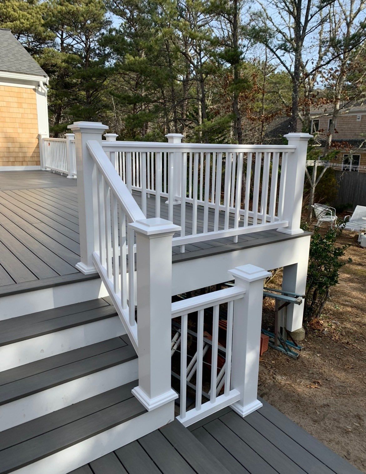 White porch staircase with railings and steps leading to a deck, beside a house in a wooded yard