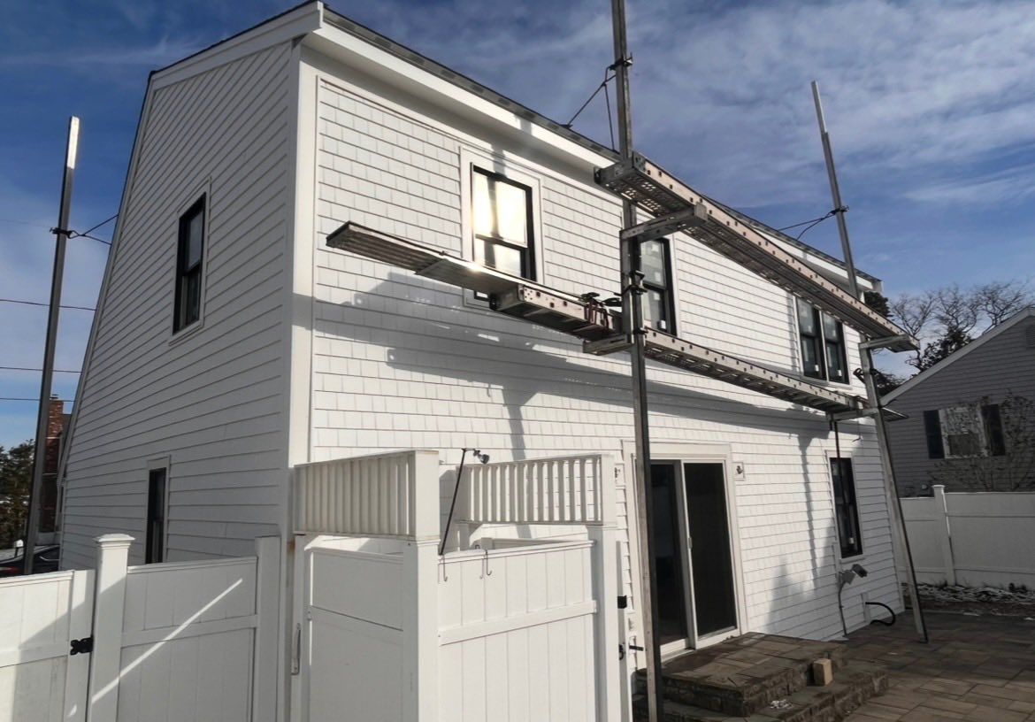White two-story house with small fenced yard and utility poles under a clear sky