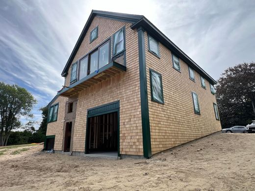 Two-story brick building with green trim and a steep roof, viewed from a low angle on a sandy lot.