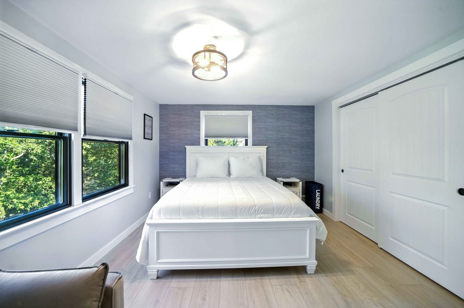Bright bedroom with white bed, closet doors, and windows with blinds on a gray-and-white wall
