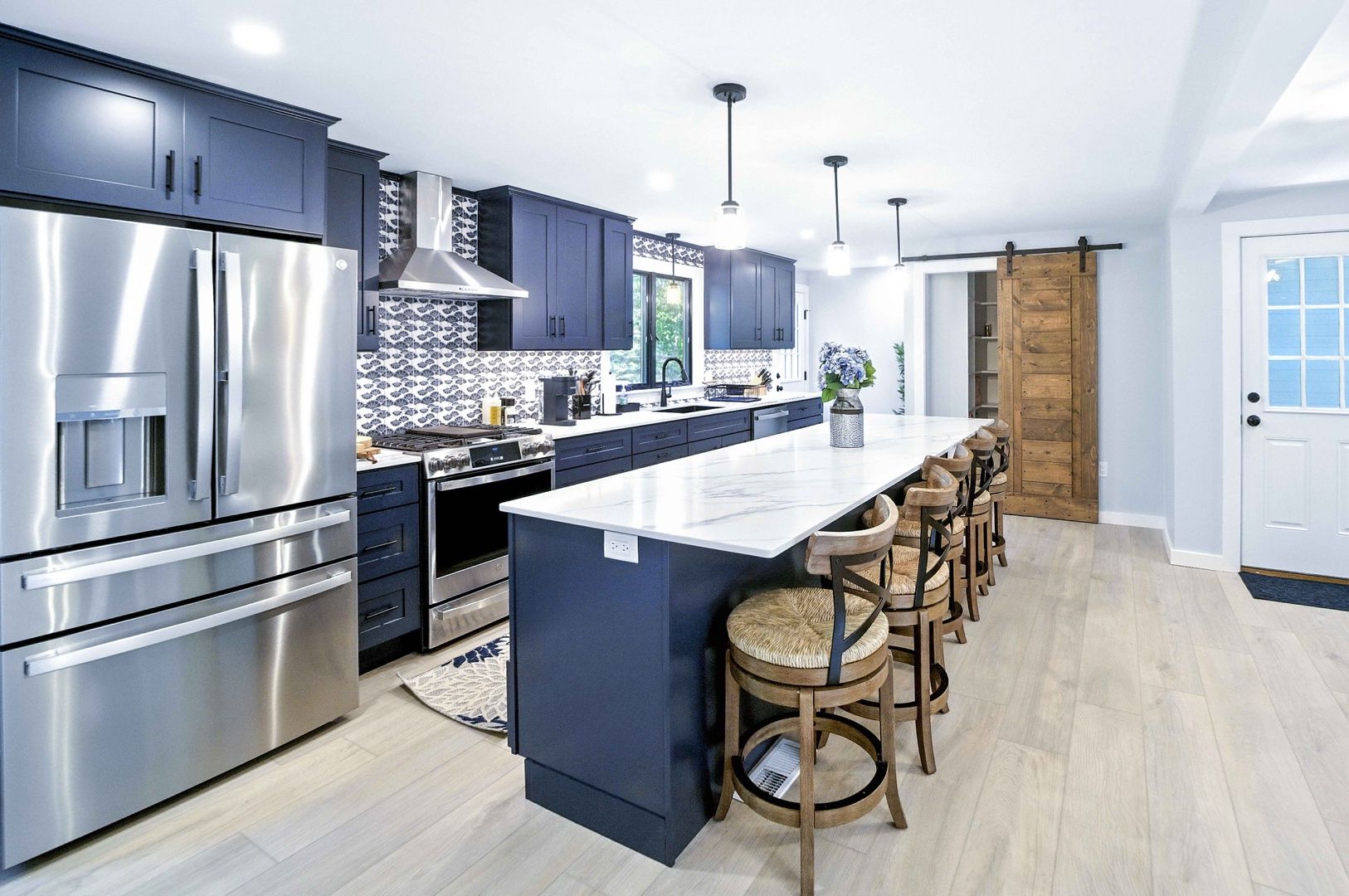 Bright modern kitchen with stainless steel appliances, island, bar stools, and light wood floors.