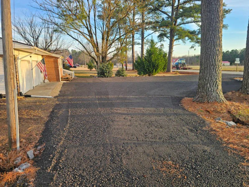 Paved driveway leading to a building with American flags; trees line the sides, a sunny day.