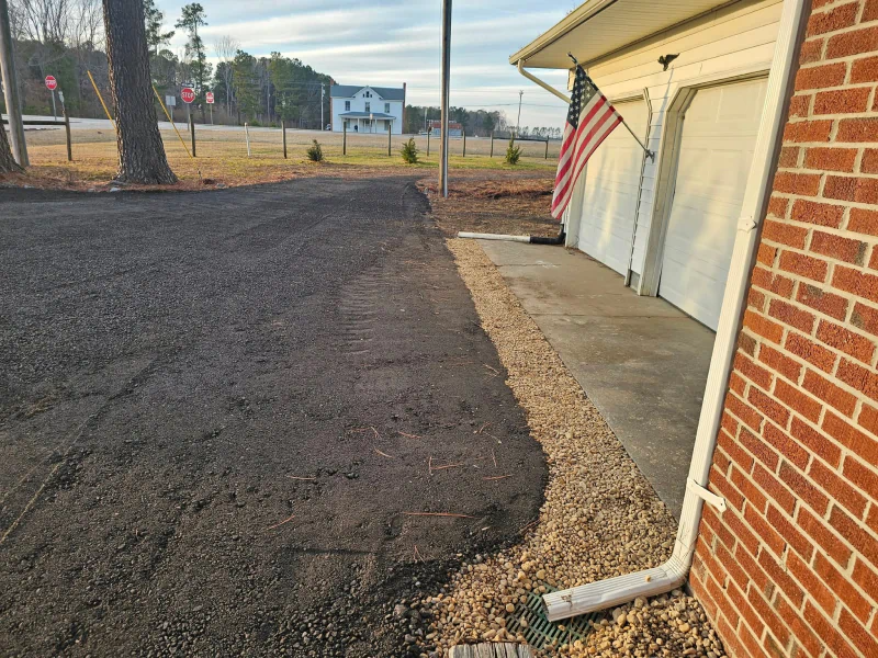 Asphalt driveway next to a gravel strip and a garage. An American flag hangs from the garage.