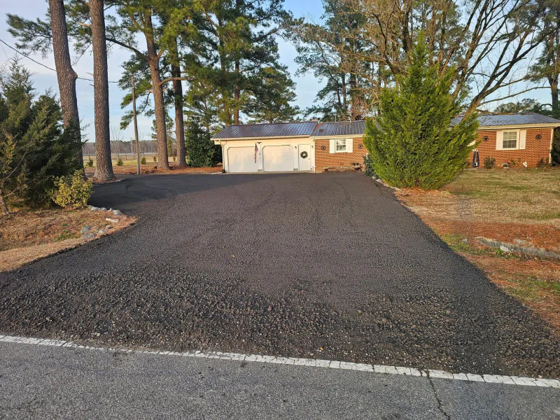 Newly paved asphalt driveway leading to a brick house with a two-car garage.