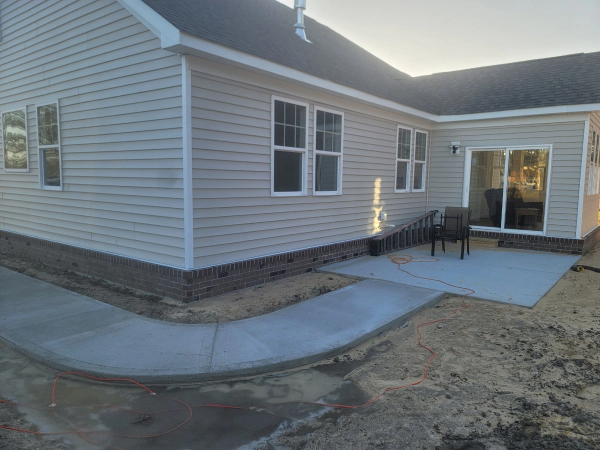 Exterior of a house with a concrete patio and walkway. Light siding with a brick base.