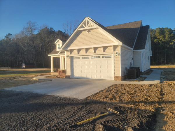 New construction, beige-sided garage with a concrete driveway and path, on a sunny day.